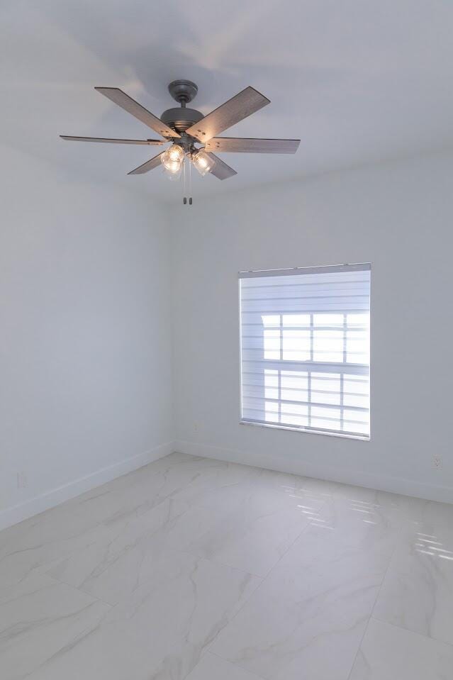 empty room with ceiling fan, marble finish floor, and baseboards