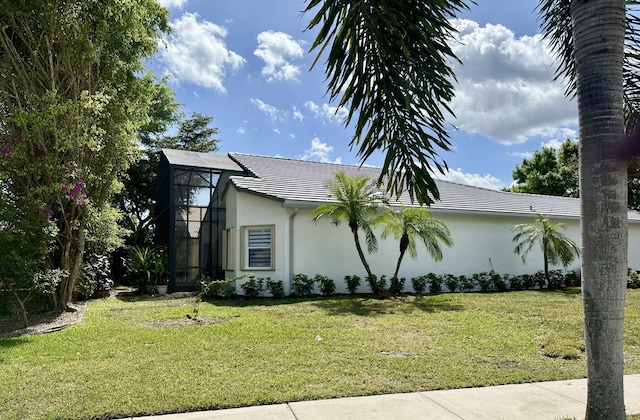 view of property exterior with stucco siding, a tiled roof, glass enclosure, and a yard
