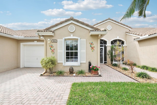 view of front of house featuring a garage, a tile roof, decorative driveway, and stucco siding