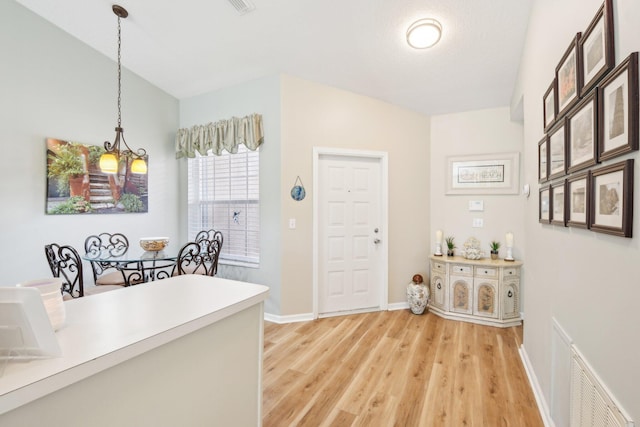 hallway with an inviting chandelier, light wood-style flooring, visible vents, and baseboards