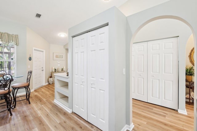 hall with light wood-style floors, baseboards, and visible vents