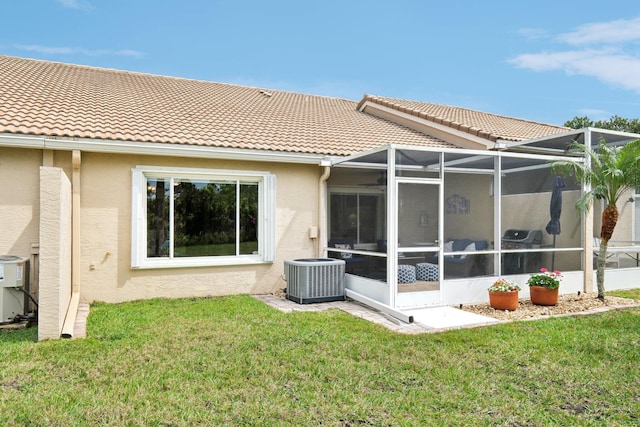 rear view of house with central AC unit, a lawn, glass enclosure, a tile roof, and stucco siding