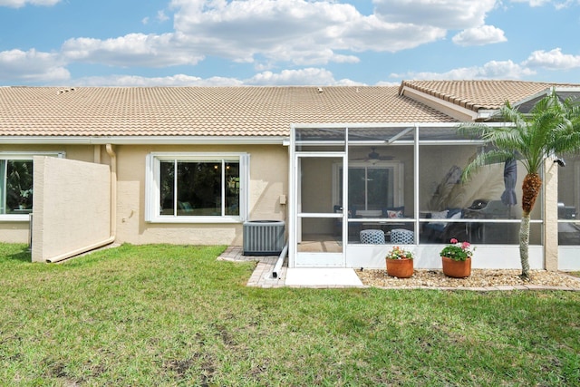 rear view of house with stucco siding, a yard, a tiled roof, and central AC unit