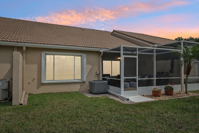 back of house at dusk with central AC, a lawn, a tiled roof, and stucco siding