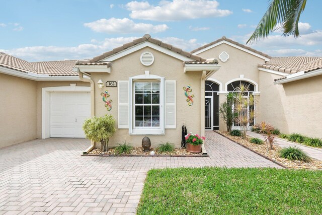 view of exterior entry with a garage, decorative driveway, a tile roof, and stucco siding