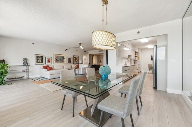 dining space featuring a textured ceiling, baseboards, and light wood-style floors