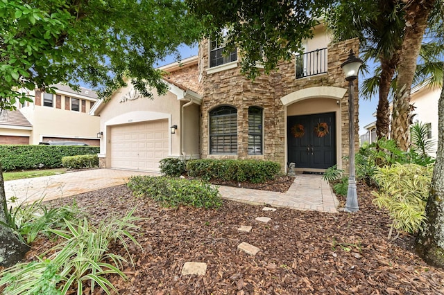 view of front of home featuring a garage, driveway, a balcony, stone siding, and stucco siding