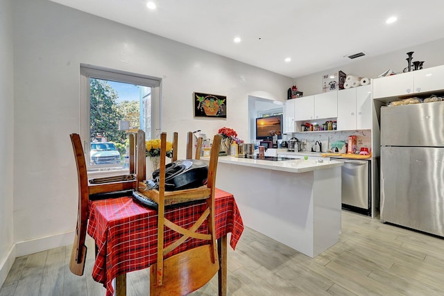 kitchen with white cabinetry, light countertops, appliances with stainless steel finishes, decorative backsplash, and light wood finished floors