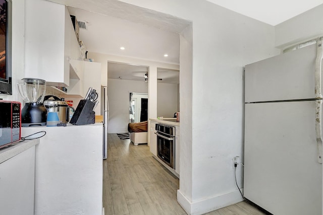 kitchen with light wood-type flooring, stainless steel oven, light countertops, and freestanding refrigerator