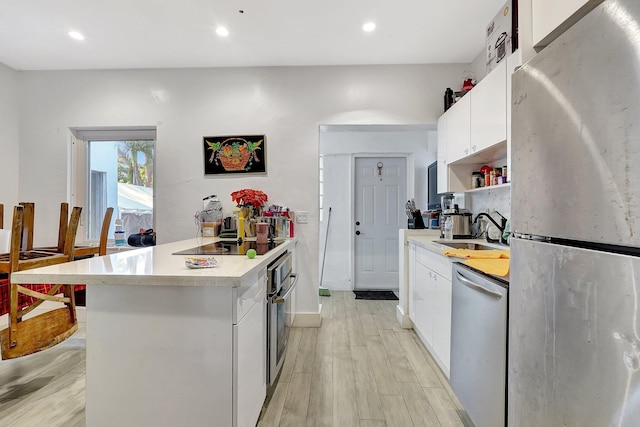 kitchen with a peninsula, a sink, white cabinets, light countertops, and appliances with stainless steel finishes