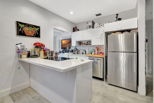 kitchen featuring stainless steel appliances, white cabinetry, light wood-style floors, light countertops, and tasteful backsplash