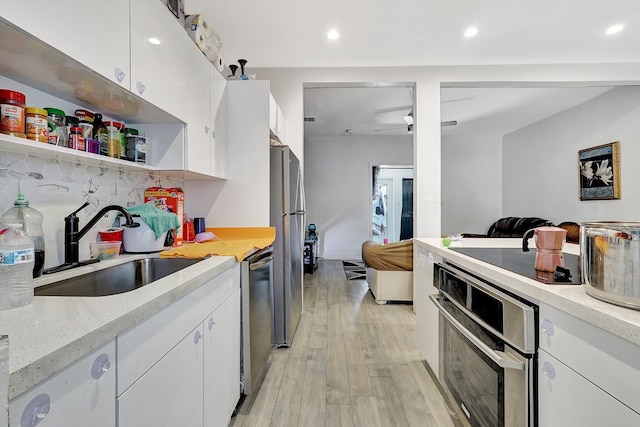 kitchen featuring stainless steel appliances, white cabinets, a sink, and light wood-style flooring