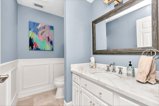 bathroom with toilet, wainscoting, visible vents, a decorative wall, and vanity