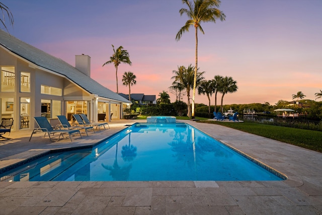 pool at dusk featuring a pool with connected hot tub and a patio