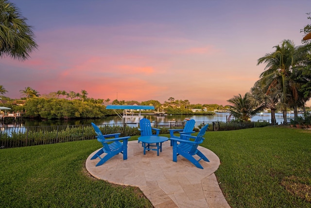 patio terrace at dusk with a yard, a water view, and fence