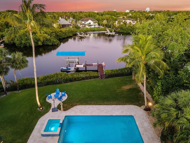 pool at dusk with a lawn, a boat dock, boat lift, and a water view