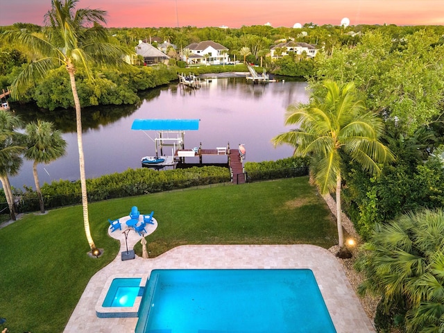 pool at dusk featuring a water view, a boat dock, boat lift, a lawn, and a pool with connected hot tub