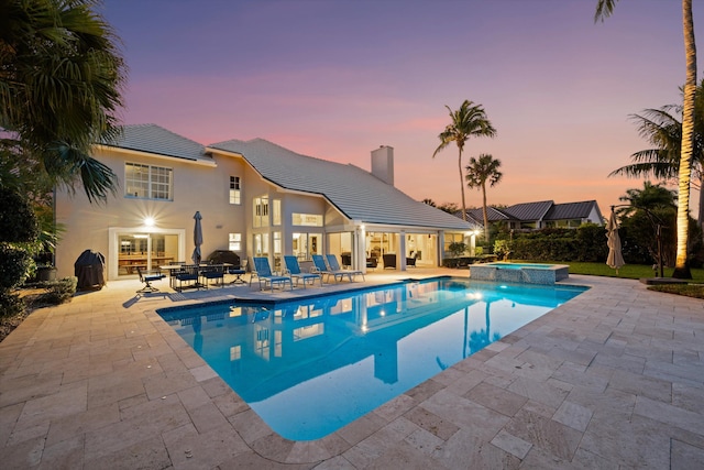 pool at dusk with a pool with connected hot tub and a patio
