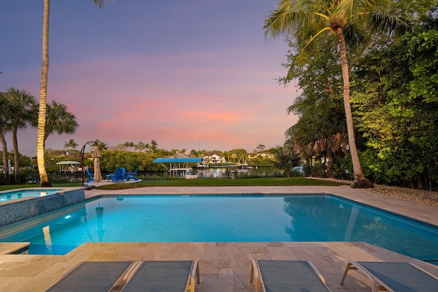 pool at dusk featuring a pool with connected hot tub and fence
