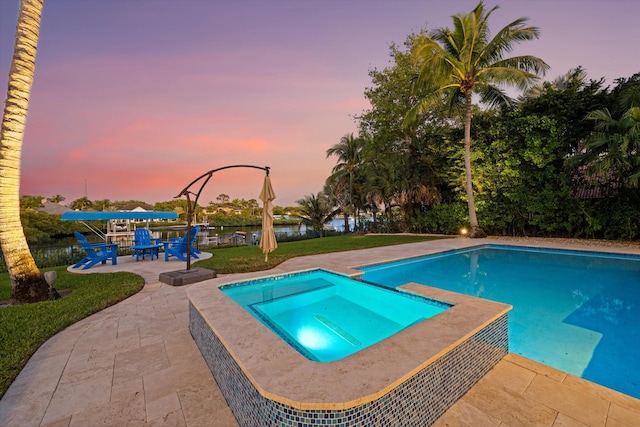 pool at dusk with a yard, a patio area, and a pool with connected hot tub