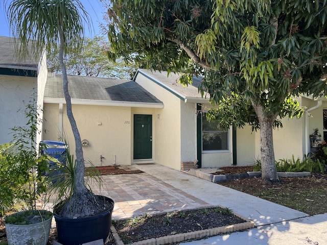 view of exterior entry with roof with shingles and stucco siding