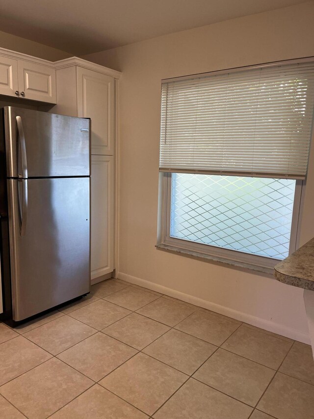 kitchen featuring light tile patterned floors, baseboards, freestanding refrigerator, and white cabinets