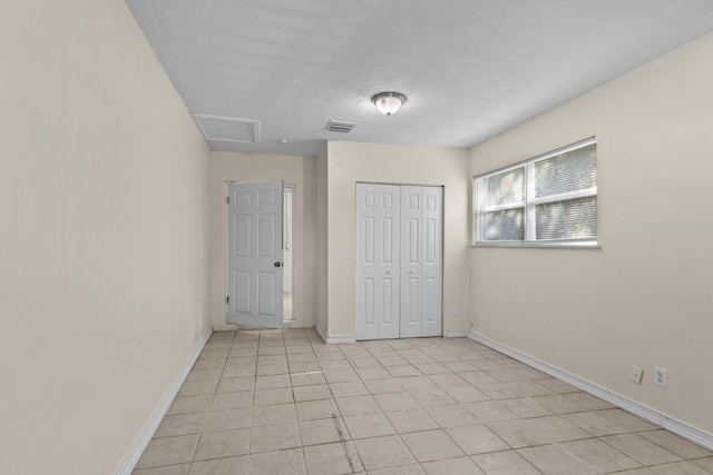 unfurnished bedroom featuring a closet, visible vents, attic access, a textured ceiling, and baseboards