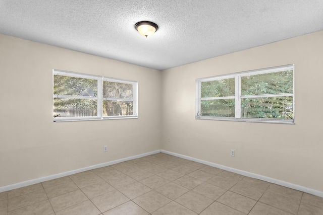 spare room with a textured ceiling, light tile patterned floors, and baseboards