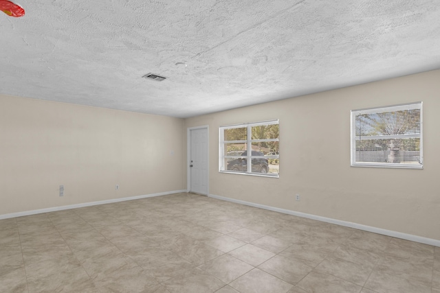 empty room featuring visible vents, a textured ceiling, and baseboards