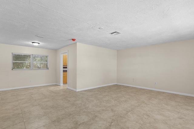 spare room featuring baseboards, visible vents, and a textured ceiling