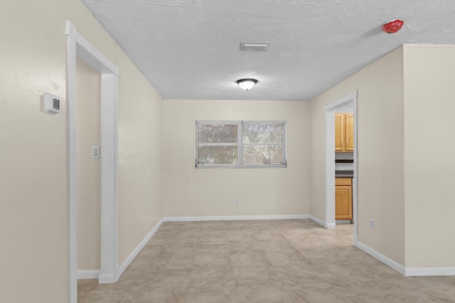 unfurnished room with a textured ceiling, visible vents, and baseboards