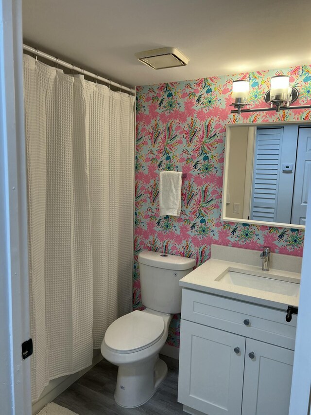 bathroom with wood finished floors, vanity, toilet, and wallpapered walls