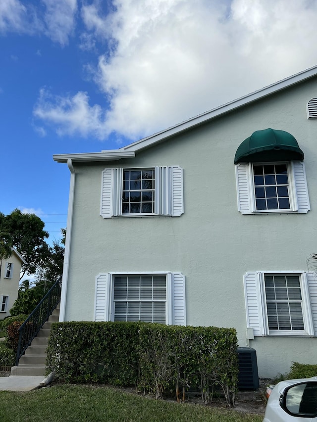 view of property exterior featuring central AC, stairway, and stucco siding