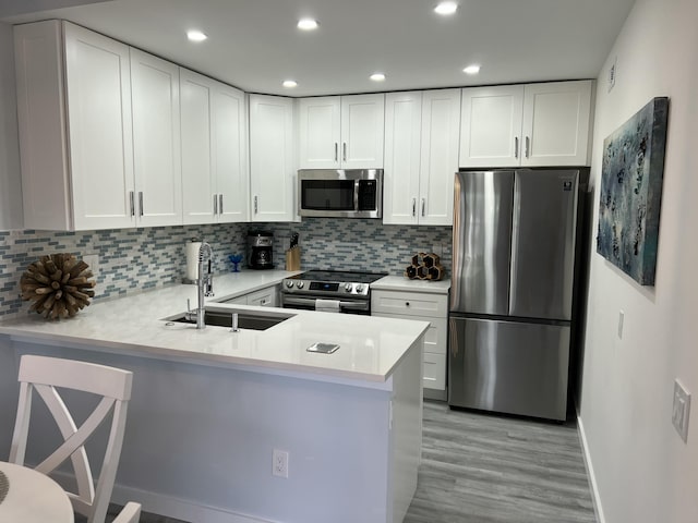 kitchen with stainless steel appliances, a peninsula, a sink, white cabinets, and light countertops