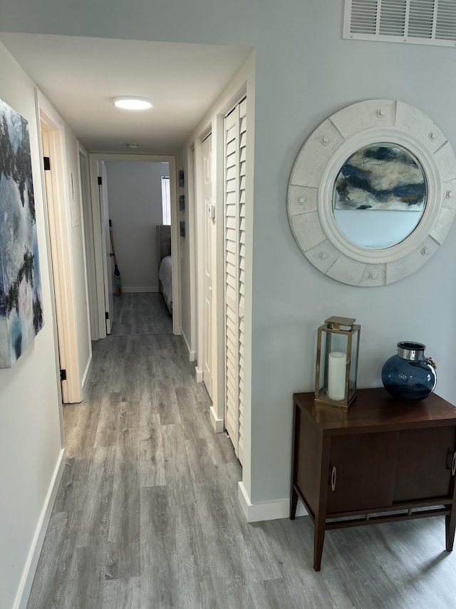 hall with visible vents, baseboards, and wood finished floors