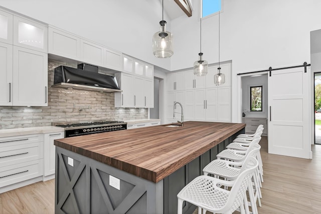 kitchen featuring wooden counters, a barn door, a sink, gas range, and wall chimney exhaust hood