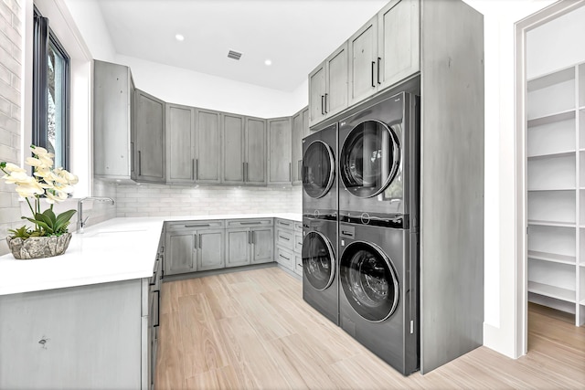 laundry room with stacked washer / dryer, a sink, visible vents, cabinet space, and light wood finished floors