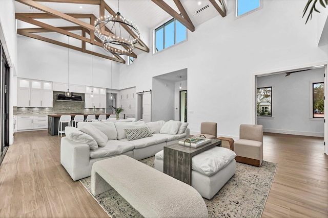 living room with light wood-style floors, a chandelier, lofted ceiling with beams, and baseboards