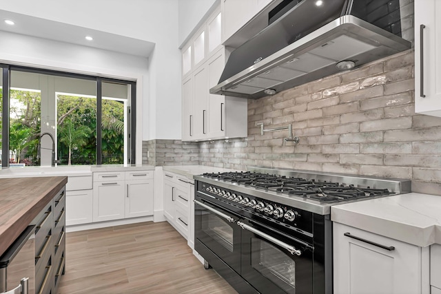 kitchen with under cabinet range hood, butcher block countertops, white cabinetry, double oven range, and tasteful backsplash