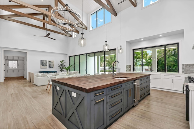 kitchen with a kitchen island with sink, a sink, light wood-style floors, white cabinets, and wooden counters