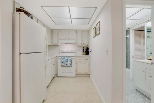 kitchen featuring white appliances, light countertops, under cabinet range hood, and baseboards