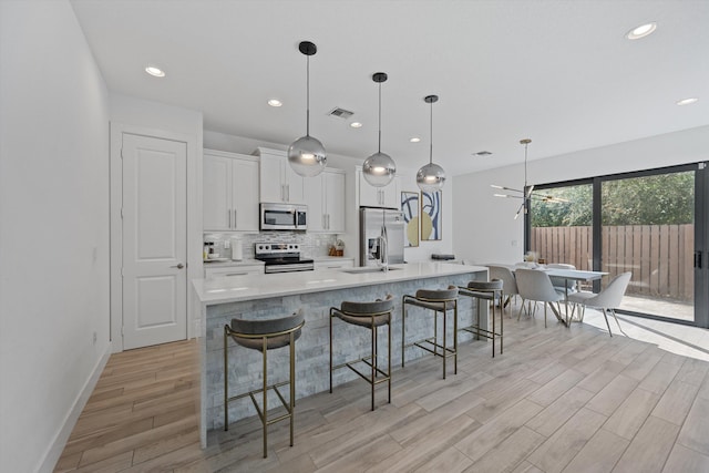 kitchen featuring stainless steel appliances, light countertops, decorative backsplash, white cabinets, and a large island with sink