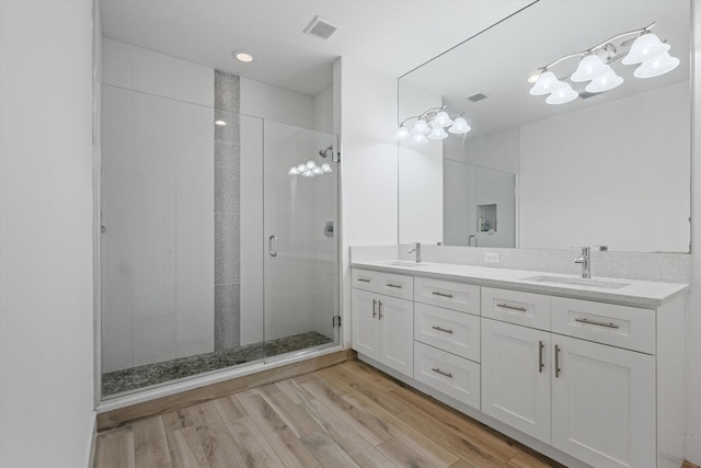 bathroom with wood finished floors, a sink, visible vents, a shower stall, and double vanity