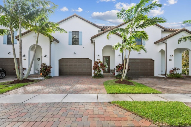 mediterranean / spanish-style house featuring a garage, decorative driveway, a tile roof, and stucco siding