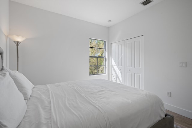 bedroom with a closet, visible vents, baseboards, and wood finished floors