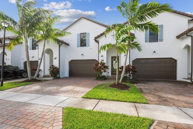 mediterranean / spanish-style home with a garage, decorative driveway, a tiled roof, and stucco siding