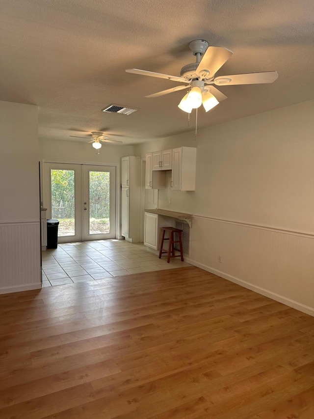 unfurnished living room with light wood-style floors, a textured ceiling, french doors, and wainscoting