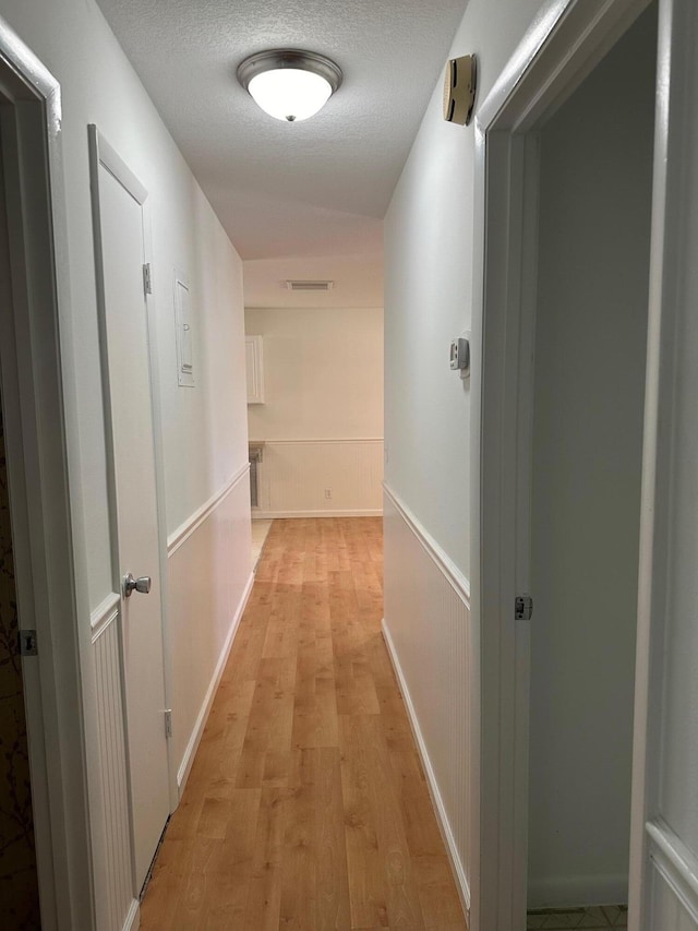 hallway with light wood-type flooring, visible vents, and a textured ceiling