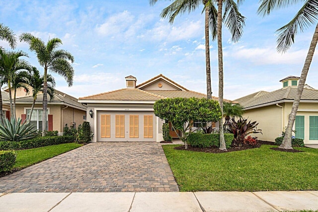 view of front of home featuring decorative driveway, a tile roof, stucco siding, a front yard, and a garage