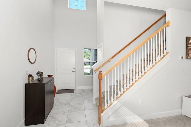 foyer featuring stairs, marble finish floor, a towering ceiling, and baseboards